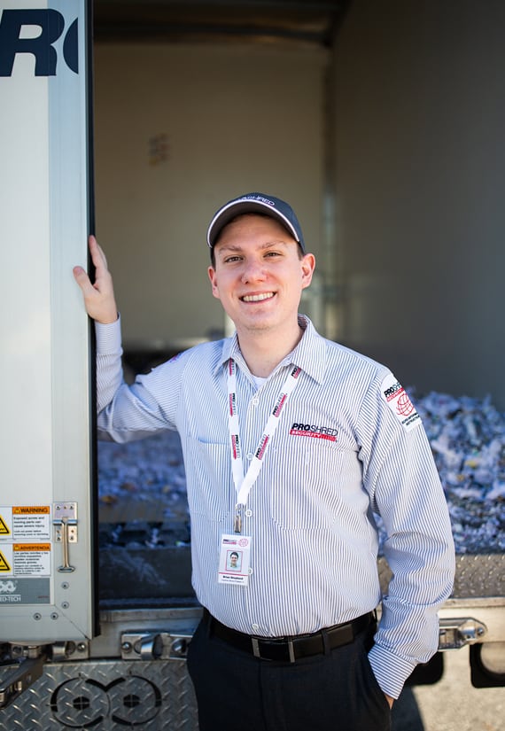 Shredding services employee standing in front of shredded paper documents.