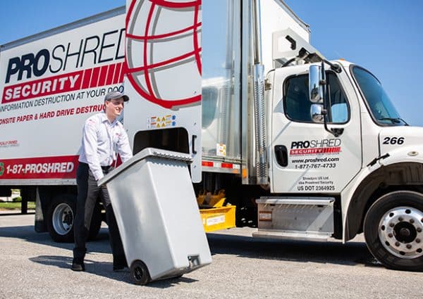 Shredding company employee pushing a 96-gallon shredding bin to a mobile shredding truck.