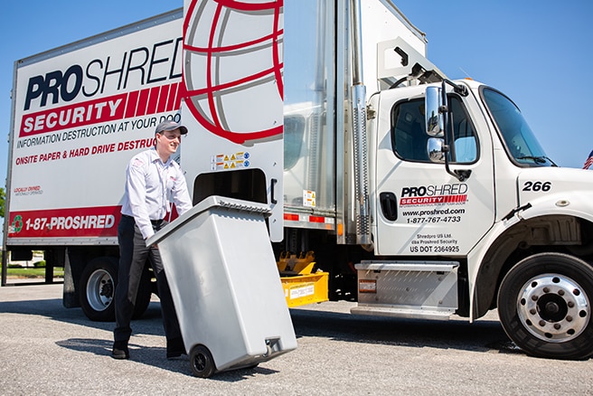 Shredding company employee pushing a 96-gallon shredding bin to a mobile shredding truck.