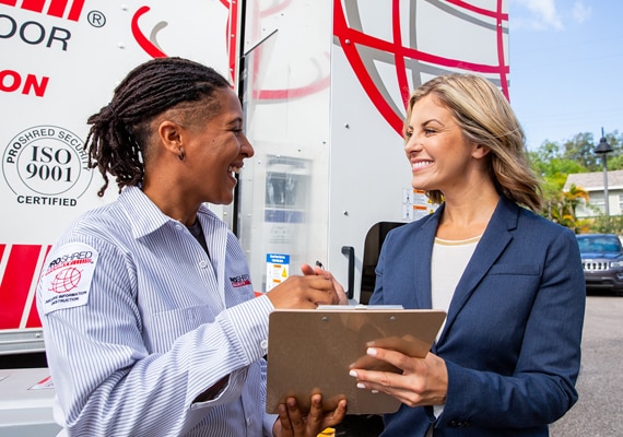 PROSHRED Security employee and business woman discussing a contract near a shredding truck.