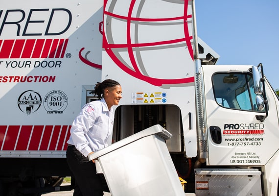 Shredding company employee pushing a bin of papers to a mobile shredder on a truck.