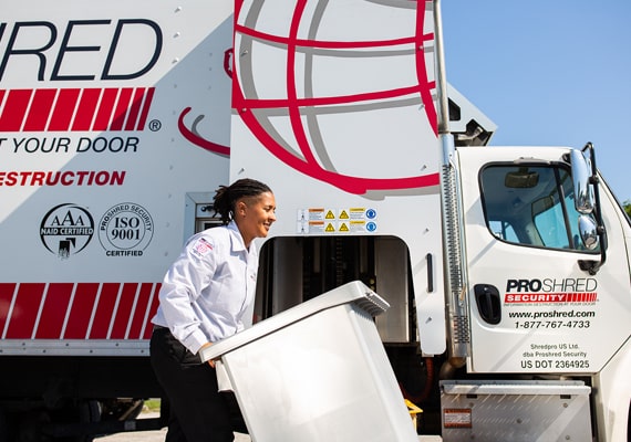 Female PROSHRED shredding employee pushing a shredding console near a truck outdoors.