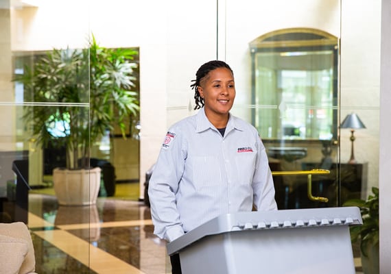 Female PROSHRED employee pushing a shredding bin outside an office.