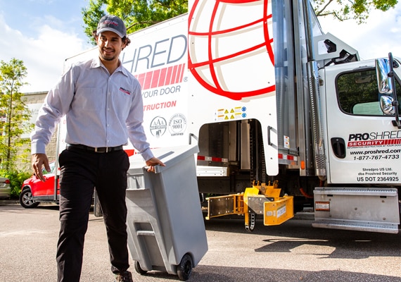 PROSHRED employee pulling a bin near a truck outdoors.