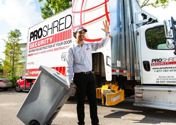 Document destruction professional pushing a shredding bin outdoors near a truck.