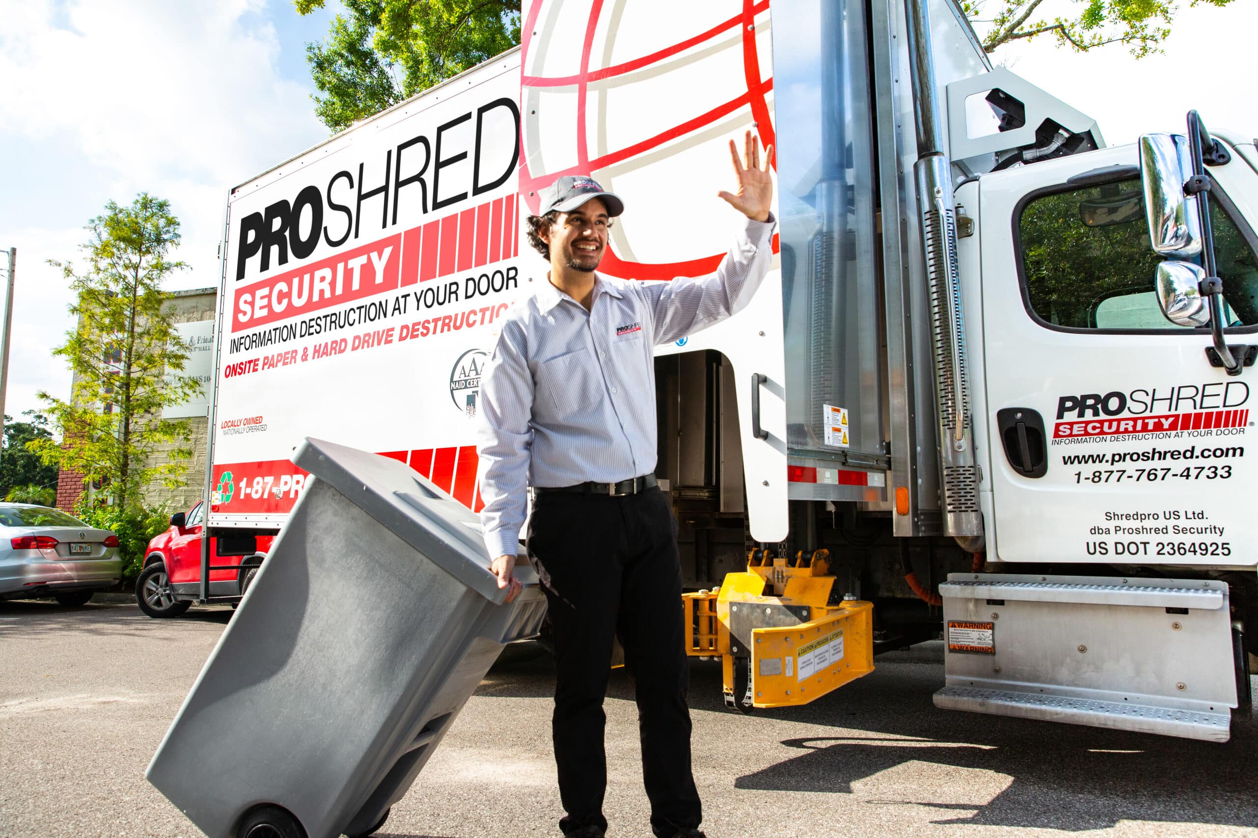 Document destruction professional pushing a shredding bin outdoors near a truck.