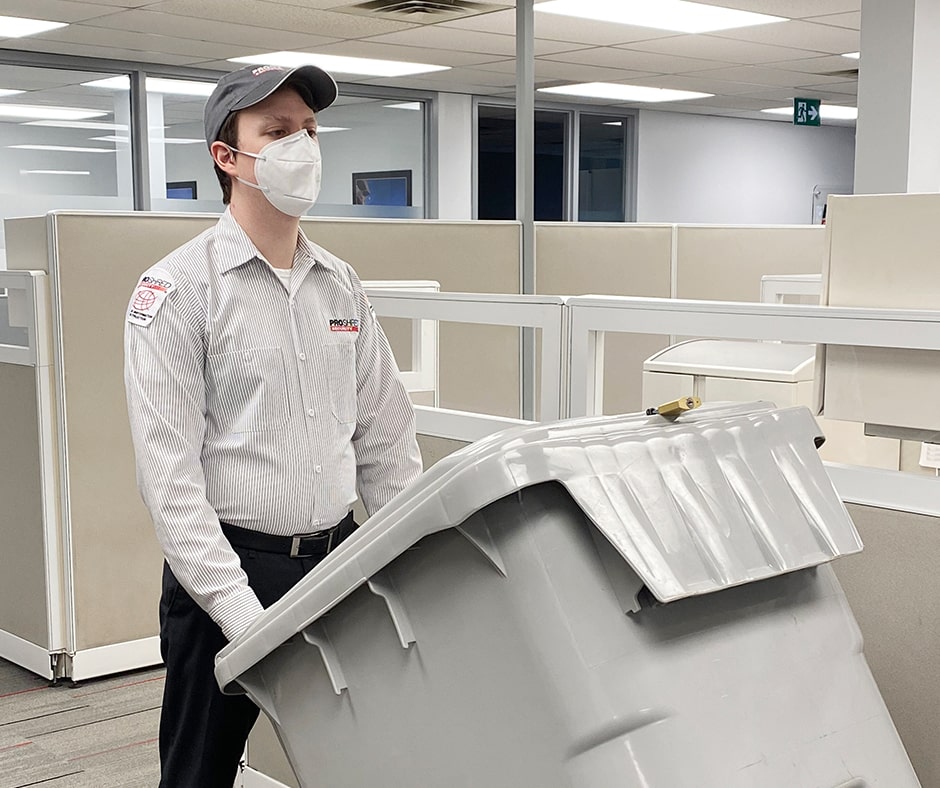 PROSHRED employee wearing a mask and pushing a bin through an office.