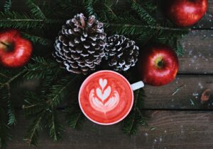 a red latte surrounded by christmas themed pine cones and cranberries