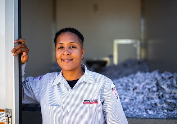 Female shredding company employee posing in front of shredded papers in a warehouse.