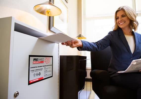 Female businessperson inserting papers into a shredding console in an office.