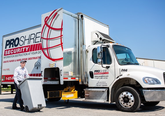 PROSHRED employee wheeling a shredding bin to a mobile shredding truck.