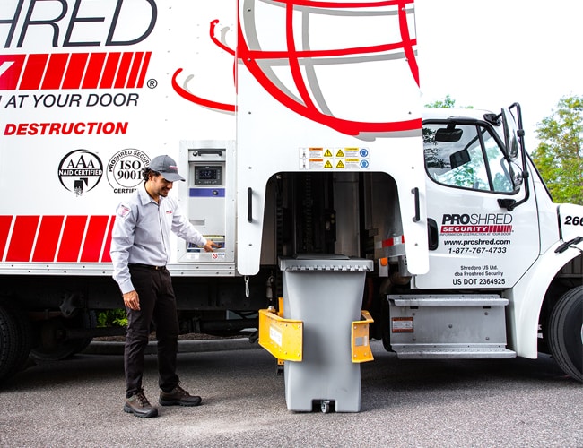 PROSHRED employee loading a security bin of documents into a mobile shredding truck.