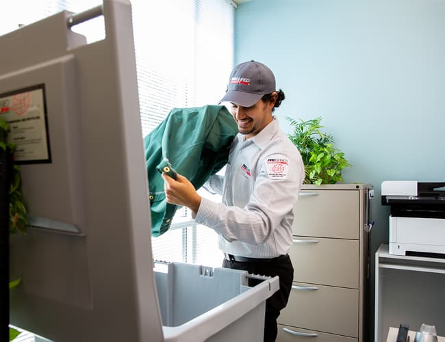 PROSHRED employee pouring office papers from a bag into a 96-gallon document shredding bin.