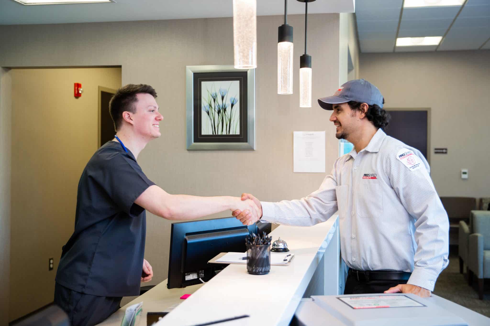 Shredding company employee and male nurse shaking hands.