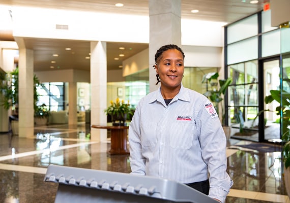 Female PROSHRED employee pushing a shredding bin containing hard drives for destruction.