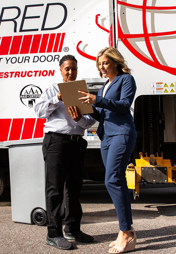 Shredding employee discussing a contract with a business woman in front of a mobile shredding truck.
