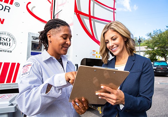 Shredding company employee and businesswoman discussing a contract outside by a mobile shred truck.