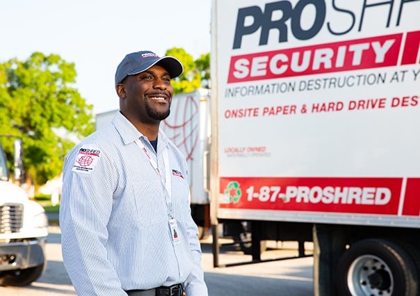 PROSHRED employee walking beside a shredding truck in a residential area.