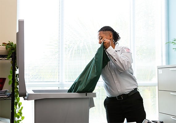 PROSHRED employee discarding the contents of a green bag into the secure console bin