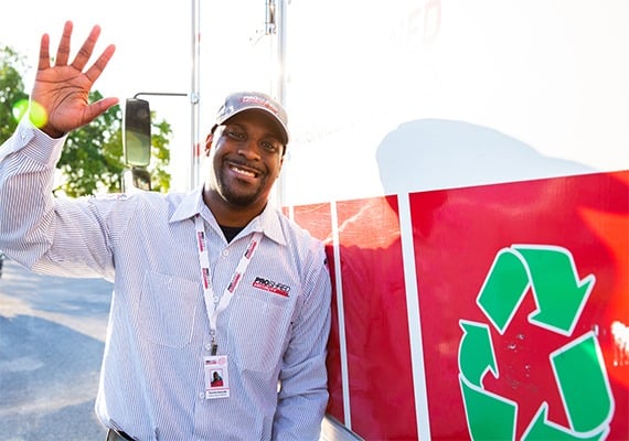 PROSHRED employee waving in front of a mobile shred truck with a recycling emblem.