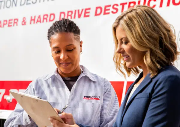 business woman signing on a clipboard next to shredding truck operator