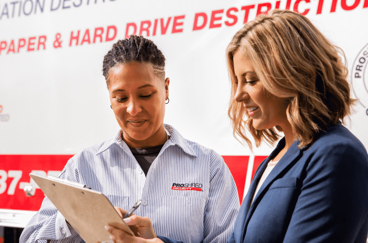 business woman signing on a clipboard next to shredding truck operator