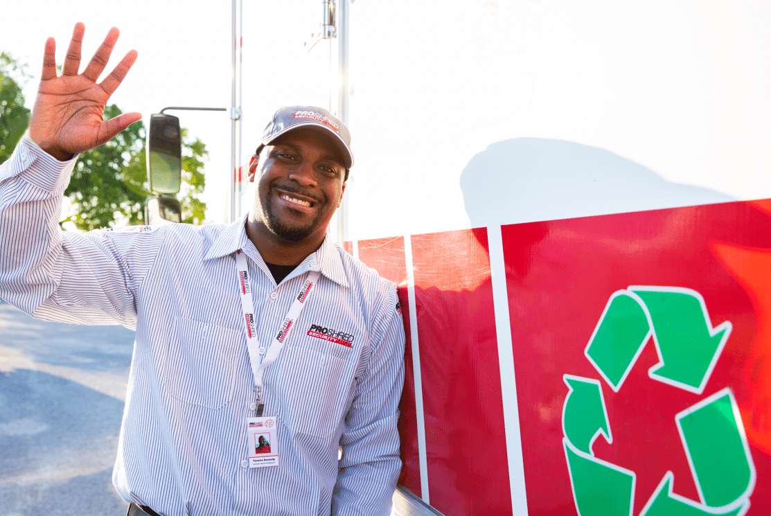 PROSHRED driver waving to the camera beside a PROSHRED shredding truck that displays a recycling logo